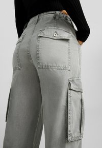 I pantaloni cargo grigi presentano una vestibilità rilassata, molteplici tasche e una texture in tessuto spazzolato. Hanno una vita alta e sono progettati con dettagli cuciti.