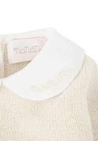 Vêtement en tricot crème avec col côtelé blanc orné du logo brodé "Nanan". La texture est douce et le design est sobre.