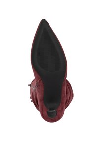 Puntige laarzen van bordeauxrood suède, gezien vanaf de zool, met een zwarte rubberen buitenzool en een klein, getextureerd hielpunt.