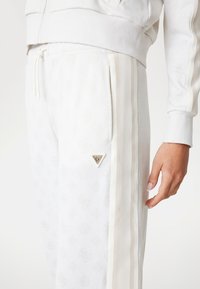 Witte sportieve broek van gestructureerde stof, met tonale patroondetails, zijstrepen en een klein metalen driehoeklogo op het linkeren been.