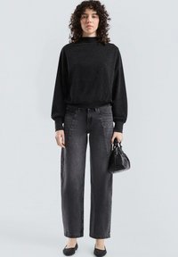 Zwarte sprankelende lange mouwen top, gecombineerd met hoge taille grijze wijde jeans. Accessoires zijn een kleine zwarte handtas en platte schoenen.