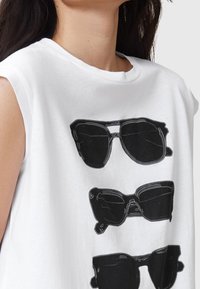 Camiseta sin mangas blanca con un estampado gráfico negro de tres gafas de sol en diferentes estilos, con textura de algodón suave y corte relajado.