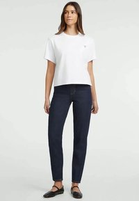 Maglietta bianca corta con maniche corte, abbinata a jeans slim-fit blu scuro. L'outfit presenta un design minimalista e un look casual.