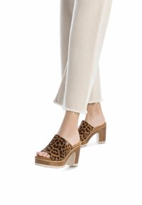 Mules de plataforma con print de leopardo y punta abierta, material de ante marrón, tacón cuadrado y suela color crema. Combinados con pantalones desgastados color crema.
