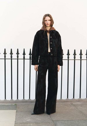 Black corduroy jacket with a brown fur collar, paired with high-waisted black flared pants. Both have a textured finish and button details.
