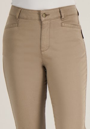 Close-up van beige broek met hoge taille, steekzakken aan de voorkant, ceintuurlussen en een knoopsluiting, gedragen met een wit topje.