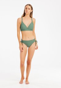 Žalias bikinis su trikampiu viršumi ir reguliuojamomis petnešėlėmis, derinamas su šoninėmis rišnosiomis kelnaitėmis. Audinys turi subtilų tekstūrinį raštą.