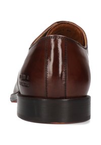 Chaussure habillée en cuir marron présentant un design élégant, une texture lisse et une semelle en caoutchouc noire. Comprend un léger détail de marque sur le talon.