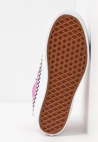 Semelle d’une chaussure avec une bande de roulement en caoutchouc marron à motif gaufré, une semelle intermédiaire blanche et une tige rose avec une bande latérale à damier noir et blanc.