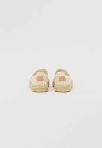 Espadrily vyrobené z ľahkej textúrovanej tkaniny s tkanou juteovou podrážkou, s malou hnedou koženou nášivkou na päte a otvoreným dizajnom vzadu.