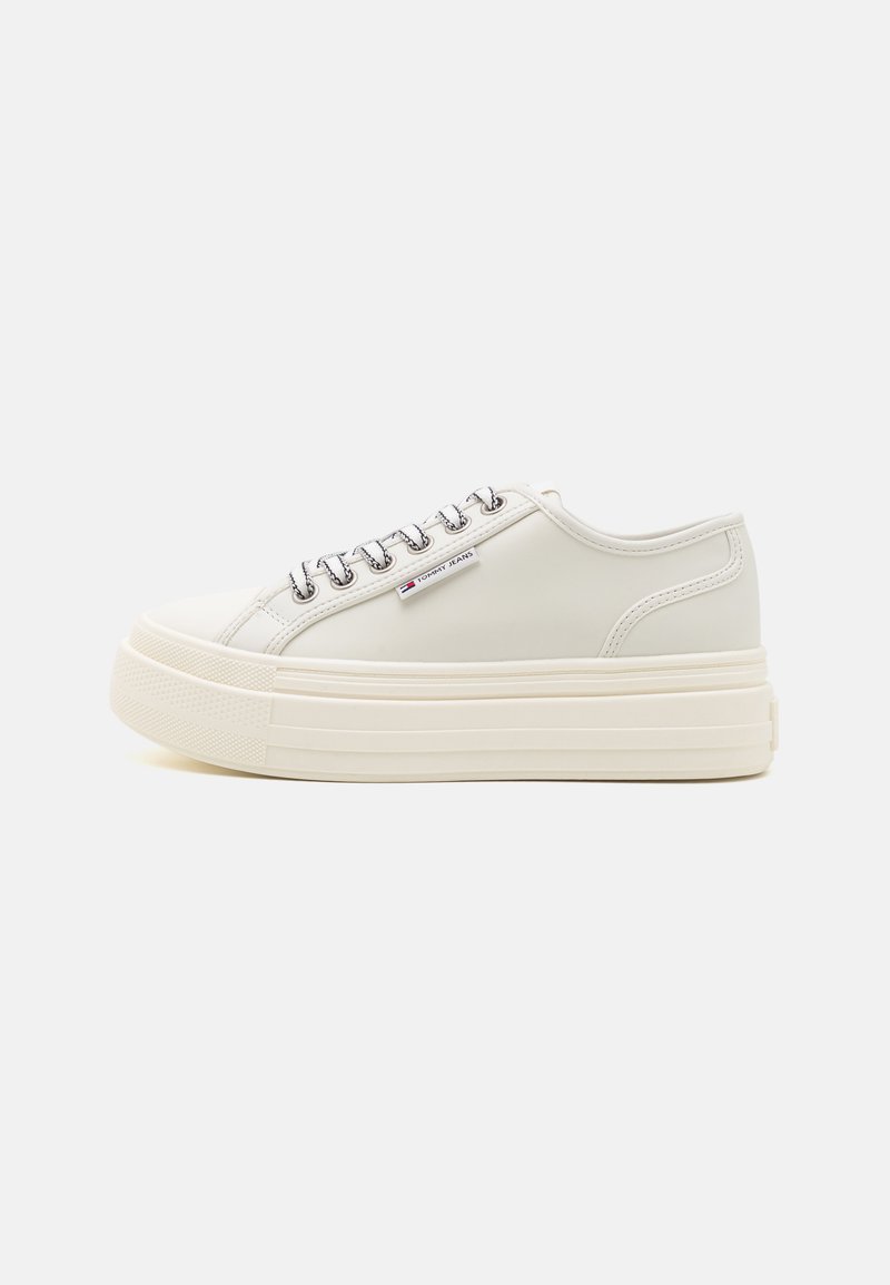 Baskets en cuir blanc avec une semelle épaisse, dotées de lacets plats, d'œillets en argent et d'un petit logo sur le côté.