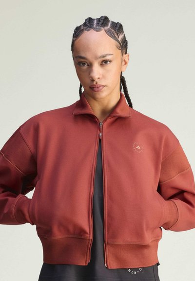 Bluza zapinana na zamek w kolorze rdzy z kołnierzem typu stójka, opuszczonymi ramionami oraz ściągaczami przy mankietach. Z przodu logo oraz boczne kieszenie.