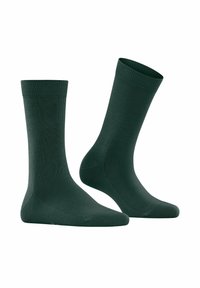 Ein Paar einfache, dunkelgrüne Kniestrümpfe, einer aufrecht und einer schräg, isoliert auf weißem Hintergrund.