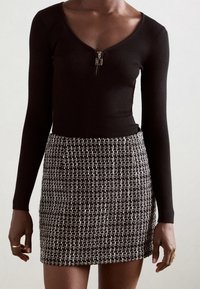 Top nero a maniche lunghe a coste con scollo zip, abbinato a una gonna corta in tessuto tricot black-and-white con motivo a griglia.