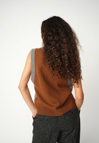 Braun und grau ärmelloser Strickpullover mit einem runden Ausschnitt, der über gerippte Details und eine weiche Textur verfügt, kombiniert mit dunklen strukturierten Hosen.
