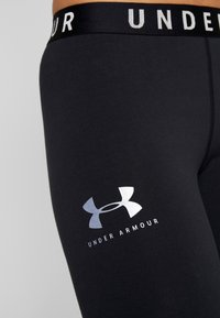 Shorts de compression noirs Under Armour avec logo sur la cuisse et ceinture de marque sur la hanche et la taille d'une personne.