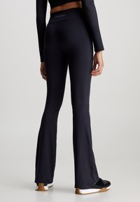 Leggings atletici neri a zampa d'elefante con vita alta, realizzati in un tessuto liscio ed elasticizzato. Logo discreto in vita, abbinati a calzature nere.