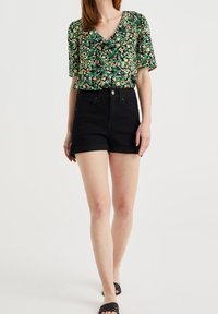 Short black denim shorts paired with a green floral blouse featuring a V-neck and short sleeves. The fabric has a textured pattern.
