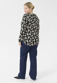 Blusa de estampado floral en negro con flores blancas, escote redondo, mangas largas y un corte holgado, combinada con jeans acampanados azul.