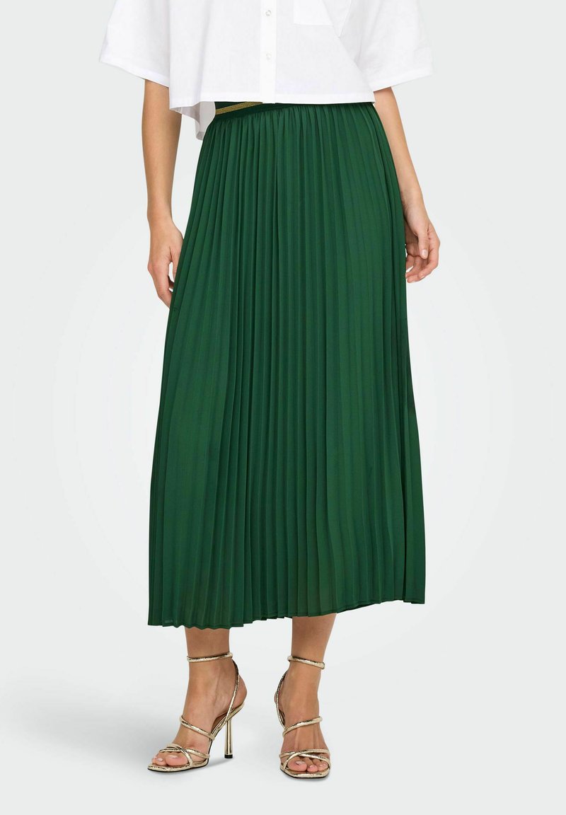Gonna maxi plissettata verde con vita elasticizzata e tessuto fluido, abbinata a sandali con tacco alto e cinturini metallici.
