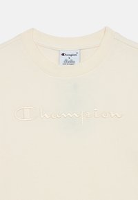 Κρεμ φούτερ με στρογγυλή λαιμόκοψη. Διαθέτει κεντημένο λογότυπο "Champion" σε ταιριαστό χρώμα. Μαλακή υφή, ελάχιστος σχεδιασμός.