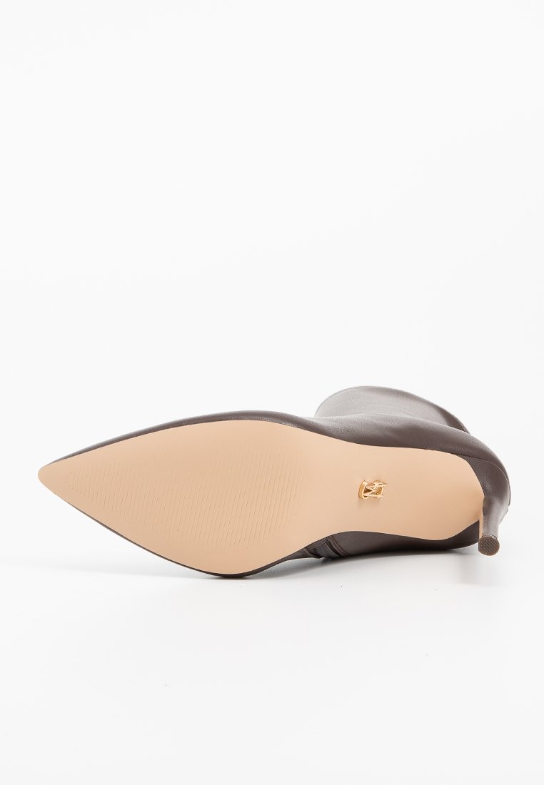 Chaussure en cuir brun à bout pointu avec un talon fin, tige texturée et une semelle beige lisse ornée d'un accento en métal doré.