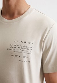 Light beige cotton t-shirt featuring printed coordinates and text in black, crew neck design, smooth texture, and short sleeves.