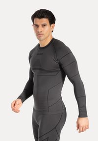 Maglia sportiva aderente a manica lunga in tessuto grigio scuro con accenti testurizzati e logo stampato, caratterizzata da un design elegante e cuciture piatte.