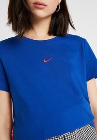 Sininen puuvillapaita lyhyillä hihoilla, jossa on punainen Nike-logo rinnassa. Paidassa on pyöreä kaula-aukko ja rento malli.