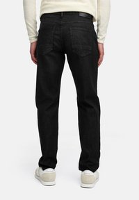 Jeans de mezclilla negros con corte recto, cinco bolsillos y un diseño liso. La cinturilla presenta una etiqueta de cuero, combinados con zapatillas blancas.