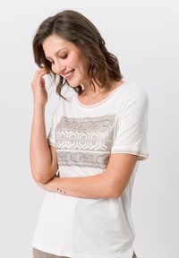 Witte t-shirt met een gemêleerd beige patroonpaneel op de borst. Korte mouwen met subtiele afwerking en een ronde halslijn. Zacht materiaal.