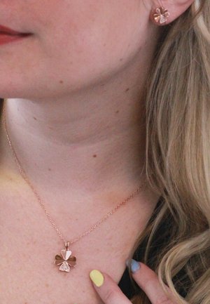 Halskette aus Roségold mit einem Kleeblatt-Anhänger, der glatte und strukturierten Blätter zeigt. Passende Ohrstecker in Form von Kleeblättern aus Roségold.