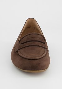 Mocassin plat en daim marron avec un bout rond, une sangle décorative sur le dessus, et une semelle beige clair, vu de face.