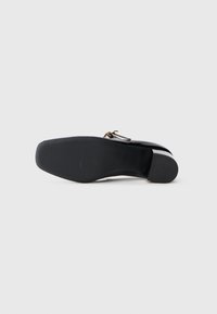 Sapato de couro preto com uma superfície lisa, bico redondo e um salto baixo empilhado. Apresenta uma fivela decorativa em tom dourado de um lado.