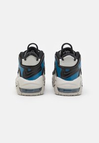 Un par de zapatillas Nike blancas, negras y azules vistas desde atrás, destacando las lengüetas de agarre y las suelas con amortiguación Air.