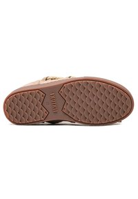 Bruine rubberen zool met een gestructureerd, golvend patroon en een ingebed logo. Het bovenmateriaal heeft een zachte beige stof met gevlochten accenten.
