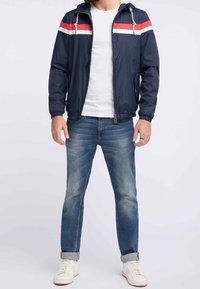 Námořnická větrovka s červenými a bílými horizontálními pruhy, se zipem, s kapucí na stažení, doplněná světle modrými džínami a bílými teniskami.