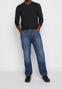 Svart långärmad henleytröja med tre knappar, matchad med ljusblå rakskurna jeans och svarta sneakers; minimalistisk design och avslappnad passform.