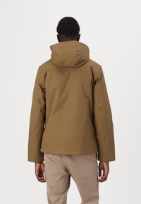 Giacca marrone con cappuccio e texture liscia, caratterizzata da un design aderente e uno stile minimalista. La vista posteriore mostra una silhouette pulita e senza hardware visibile.