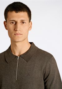 Mörkgrå zip-up polo-tröja, med en klassisk krage och präglad logotyp på vänster bröst, tillverkad av ett mjukt, texturerat tyg.