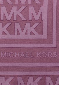 Struktureret stof i en mauve farve har gentagne "MK" logo mønstre og "MICHAEL KORS" branding i bunden, hvilket skaber et sammenhængende design.