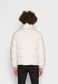 Lichtbeige pufferjack met een hoge kraag, gequilt ontwerp en elastische manchetten; heeft een gladde, glanzende afwerking en een relaxed fit.