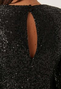 Abito nero in paillettes con chiusura a occhio di bue sul retro e scollatura rotonda. Superficie testurizzata con paillettes luccicanti in tutto l'abito.