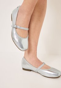 Zilverkleurige metallic balletschoenen met een ronde neus, voorzien van een dunne band en een kleine rechthoekige gesp voor aanpassing. Plat zoolontwerp.