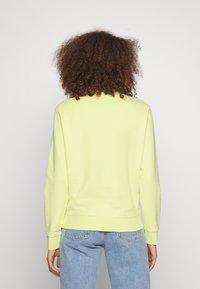 Felpa gialla brillante realizzata in tessuto morbido, con classico collo rotondo, maniche lunghe e polsini e orlo a costine. Dettaglio di cucitura sottile sul fondo.