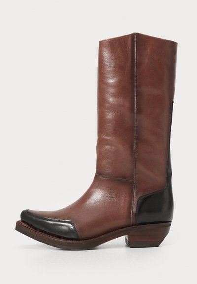 Brown leather knee-high boots featuring a pointed toe, black leather accents, and a stacked heel. Smooth texture with a sleek design.