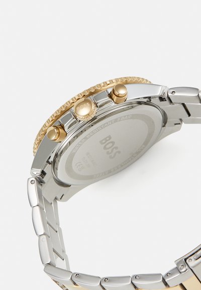Montre en acier inoxydable avec des accents dorés, boîtier rond, trois poussoirs et un bracelet en maillons poli. Résistante à l'eau jusqu'à 5 bars.