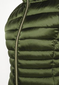 Grøn pufferjakke med en glat overflade, vandret quiltet mønster og lynlås i fuld længde foran.