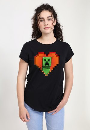 Schwarzes Baumwoll-T-Shirt mit einem pixelierten grünen Creeper innerhalb eines orangefarbenen Herzdesigns. Kurze Ärmel, lockere Passform und runder Hals.