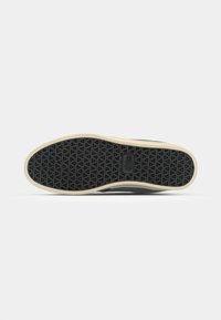 Sole di sneaker nera in gomma con un motivo a diamante, caratterizzata da un bordo color tan e una superficie testurizzata per la trazione.